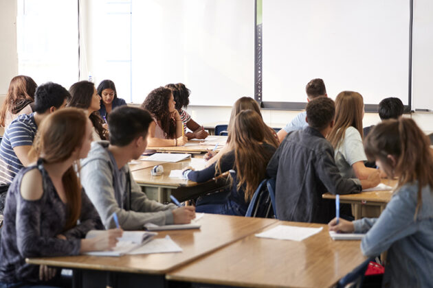 Female High School Teacher Standing By Interactive Whiteboard Teaching Lesson