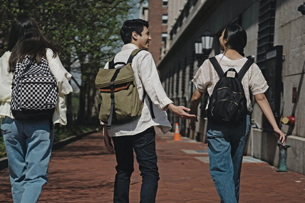 Group of three students wearing backpacks walking away down a sidewalk