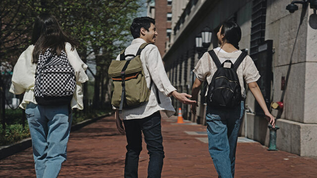 Group of three students wearing backpacks walking away down a sidewalk