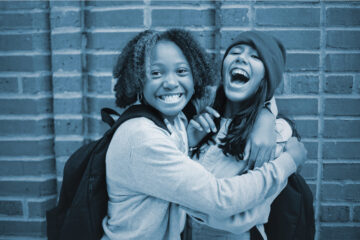 Two young girls embracing each other in front of a brick wall.