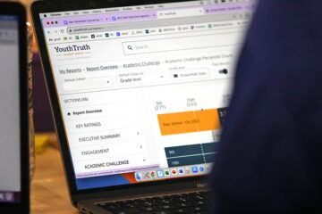A laptop screen partially obscured by the viewer's shoulder, with a YouthTruth report displayed