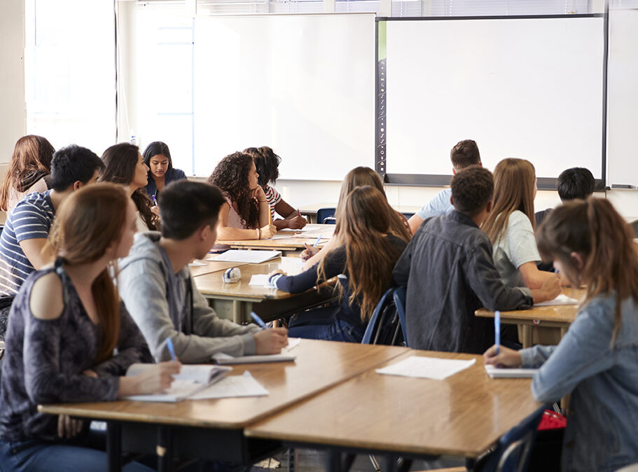 Female High School Teacher Standing By Interactive Whiteboard Teaching Lesson