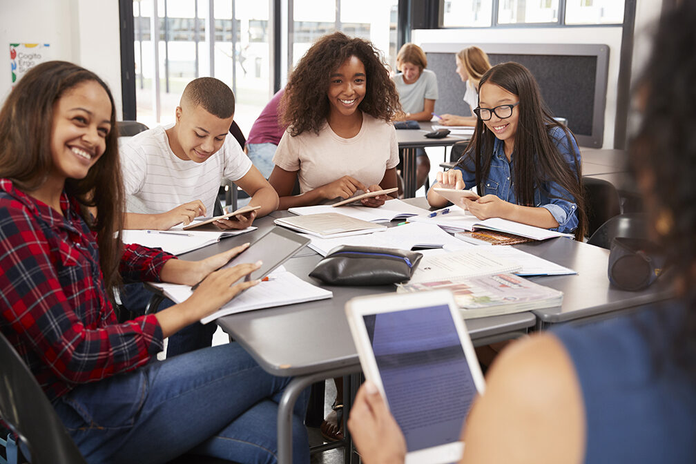 Teacher sitting with high school students using tablets