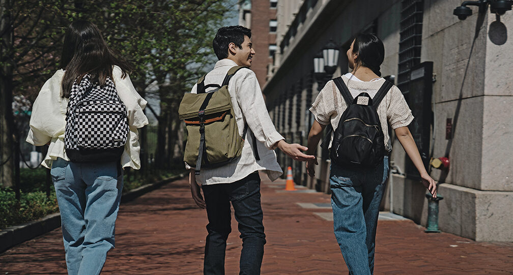 Group of three students wearing backpacks walking away down a sidewalk