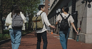Group of three students wearing backpacks walking away down a sidewalk