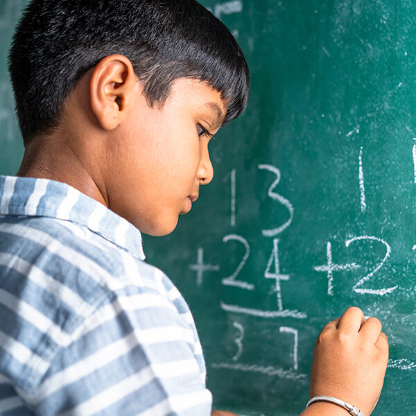 intelligent elementary school kid solving maths problem on chalkboard at classroom -concept of talented, brilliant student and education.